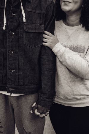 Black and white photo of couple holding hands, woman wearing engagement ring, dressed in casual denim and sweatshirt.