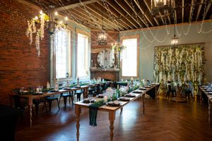 Elegant wedding reception venue with exposed brick walls, hanging greenery, chandeliers, and rustic wooden tables set for dining.