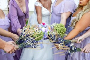 Bridesmaids in purple dresses hold wildflower bouquets with lavender and daisies at an outdoor wedding.