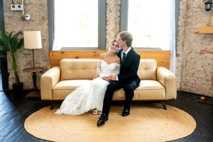 Bride and groom sit closely together on cream sofa in rustic industrial wedding venue.