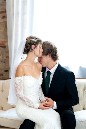 Newlyweds sharing a romantic kiss while seated on a cream sofa in a bright wedding venue.