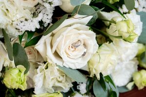 Close-up of wedding rings nestled among white roses and eucalyptus in a bridal bouquet.