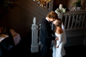 Bride and groom share an intimate forehead kiss in a dimly lit elegant wedding venue.