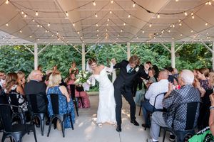 Bride and groom celebrate their ceremony exit under string lights surrounded by cheering guests.