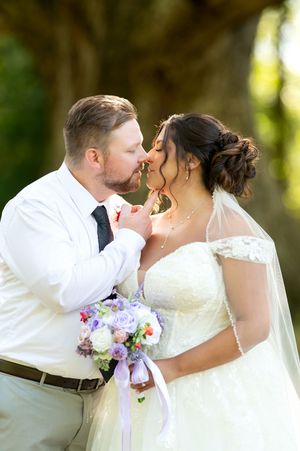 Groom tenderly holding bride's chin for a kiss while she holds a lavender and white wedding bouquet.