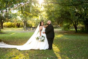 Bride and groom share a romantic moment in a sunlit garden, bride holding a white bouquet with flowing veil.