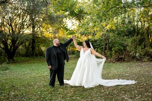 Groom twirls bride in white ball gown with long veil in a sunlit garden during outdoor wedding celebration.