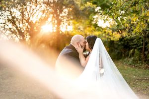 Bride and groom share a golden sunset kiss, bride's long veil flowing beautifully in the warm light.