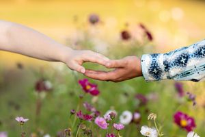 Couple gently holds hands among colorful wildflowers in a sun-drenched garden during engagement photos.