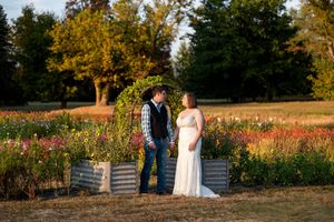 Bride and groom stand facing each other beside a flower garden arch at golden hour on their wedding day.