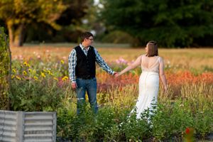 Groom leads bride by the hand through a colorful flower garden at sunset during their wedding photos.