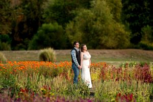 Bride and groom holding hands while walking through vibrant orange and red flower fields in autumn.