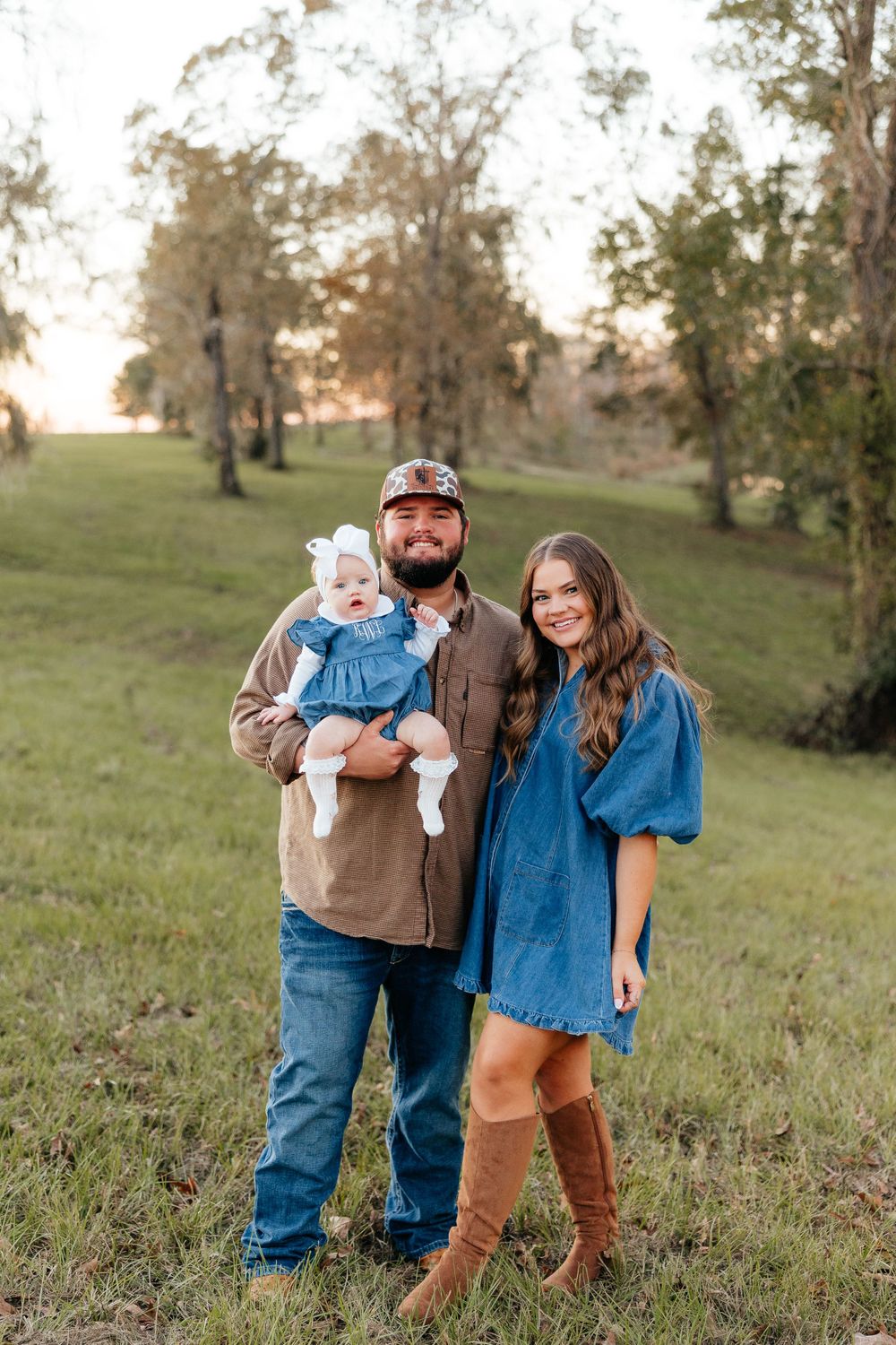 Family portrait in a scenic autumn field with warm sunset lighting.