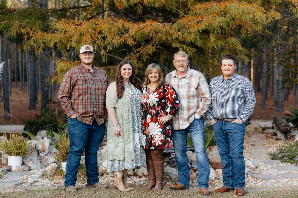 Extended family group in casual attire poses together against an autumn forest backdrop.