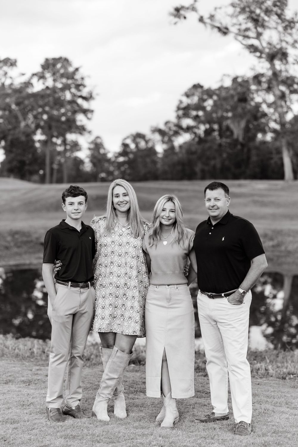 Black and white portrait of four people in coordinated outfits standing on a golf course.