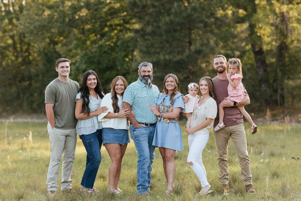 Large family group portrait smiling outdoors in a green field, including adults and young children.