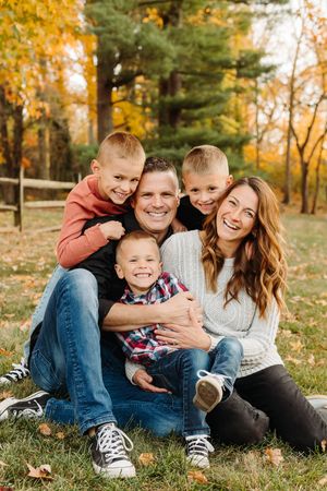 A cheerful family sits together on autumn grass surrounded by golden fall foliage in a park setting.