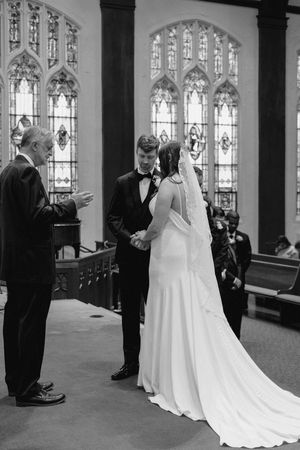 A wedding ceremony takes place in a church with Gothic stained glass windows and elegant stone columns.
