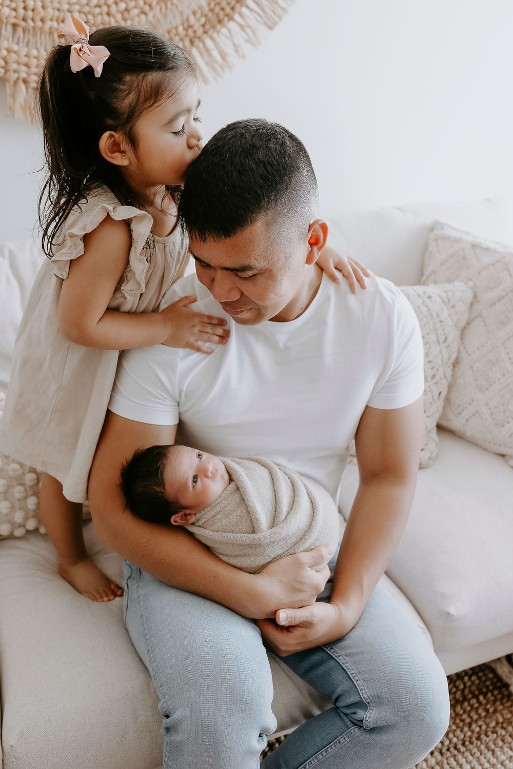 A tender family moment captured in a series of intimate black and white photographs on a white couch.