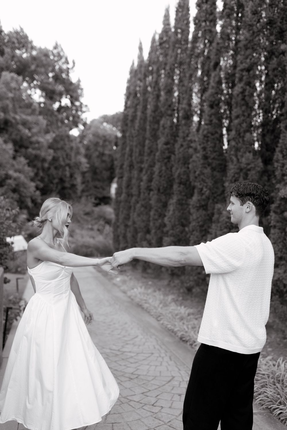 Black and white photo sequence showing couple walking and twirling together on a tree-lined path.