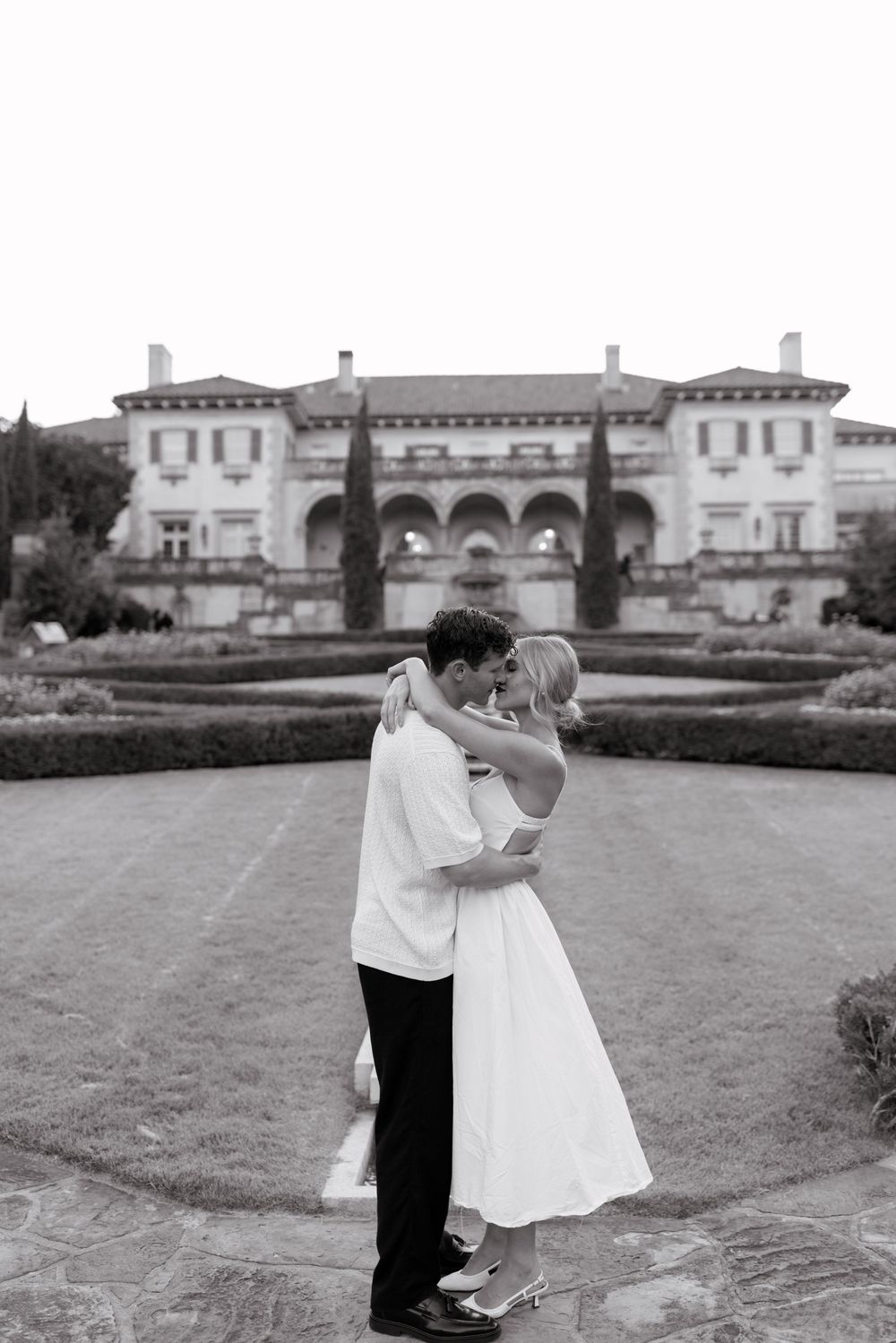 A couple shares a romantic dance moment on a grand lawn with an elegant mansion in the background.