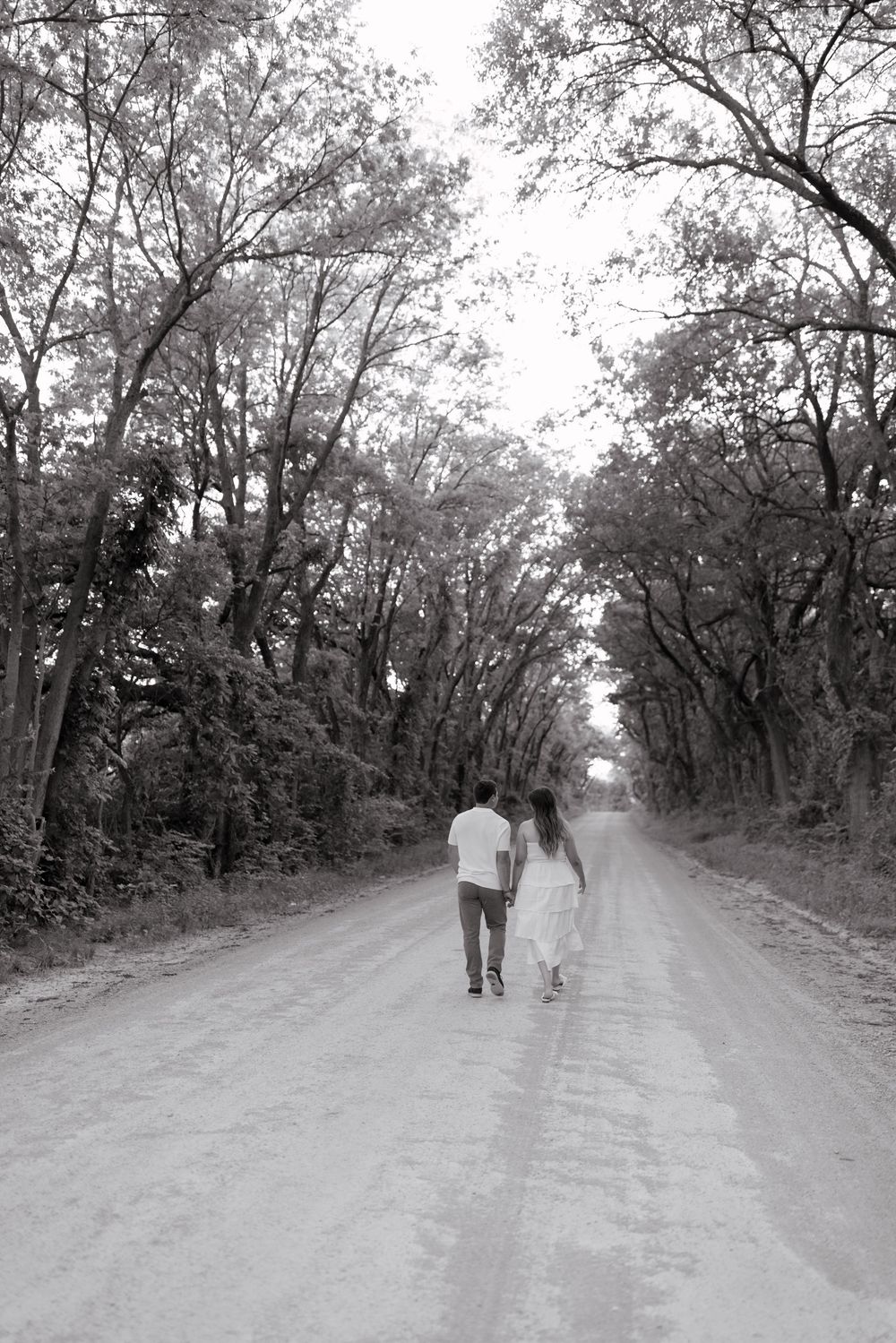 Two figures walk along a serene dirt path surrounded by trees in black and white photography.