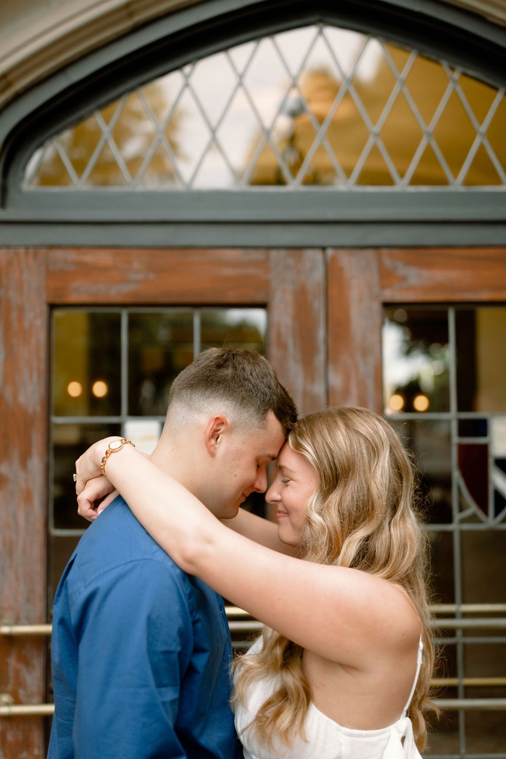 A romantic couple shares an intimate moment during their wedding dance at an elegant indoor venue with arched windows.