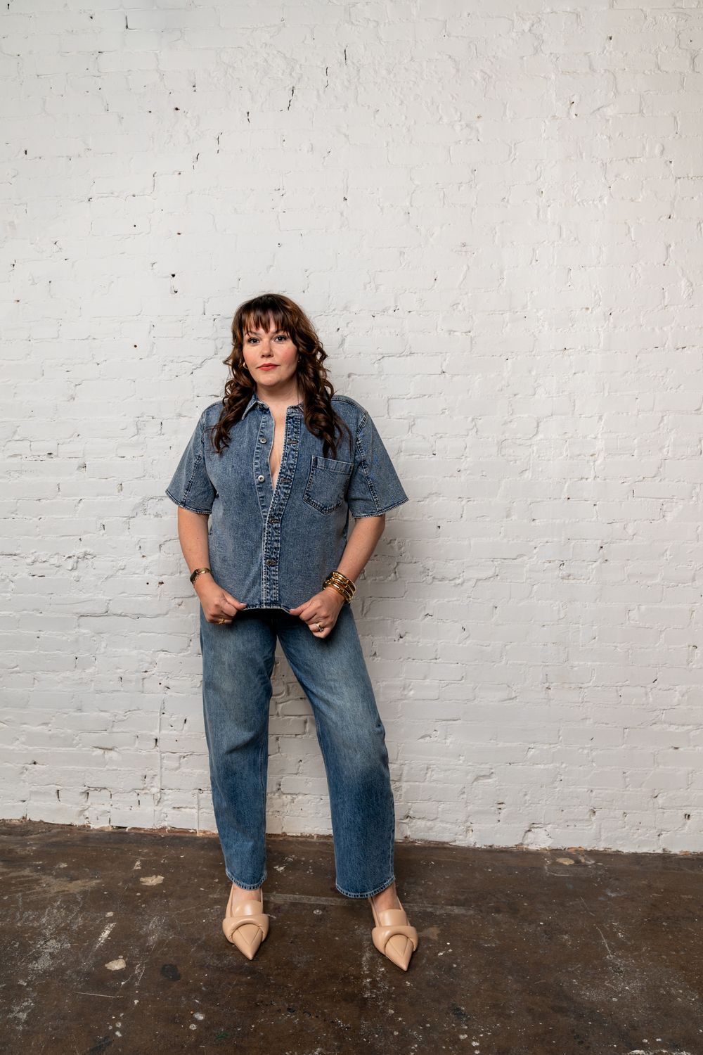 Casual denim-on-denim look with ballet flats against white brick wall in industrial space.