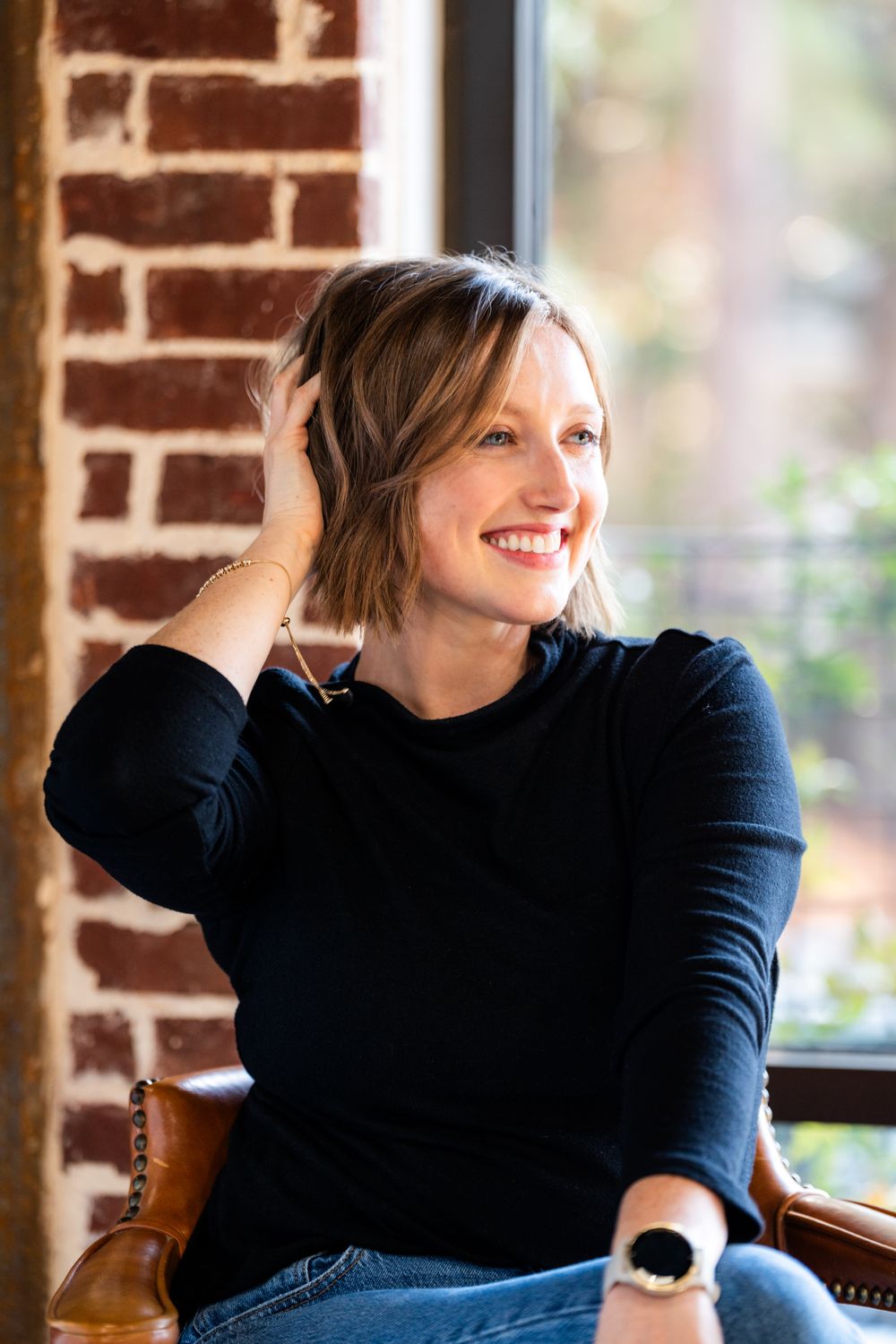 Person in black sweater seated by brick wall in natural lighting.