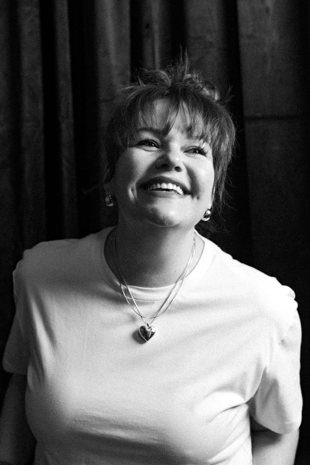 Black and white portrait showing genuine joyful laughter while wearing a white top and necklace.