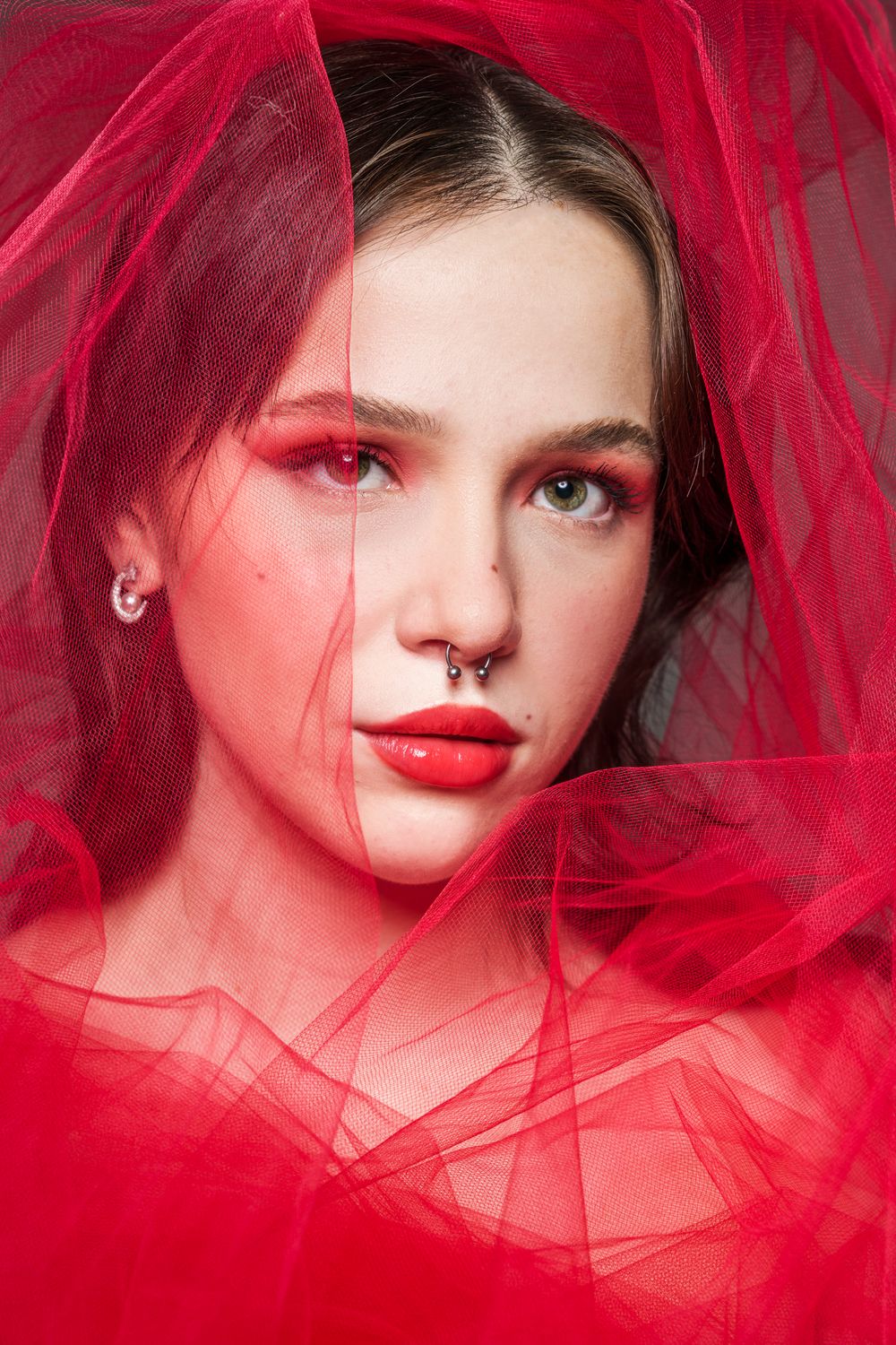 Artistic portrait with red tulle fabric creating ethereal atmosphere and dramatic lighting.