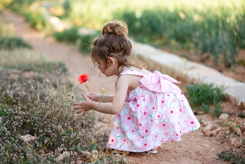 Child in pink floral dress exploring garden path on sunny day.