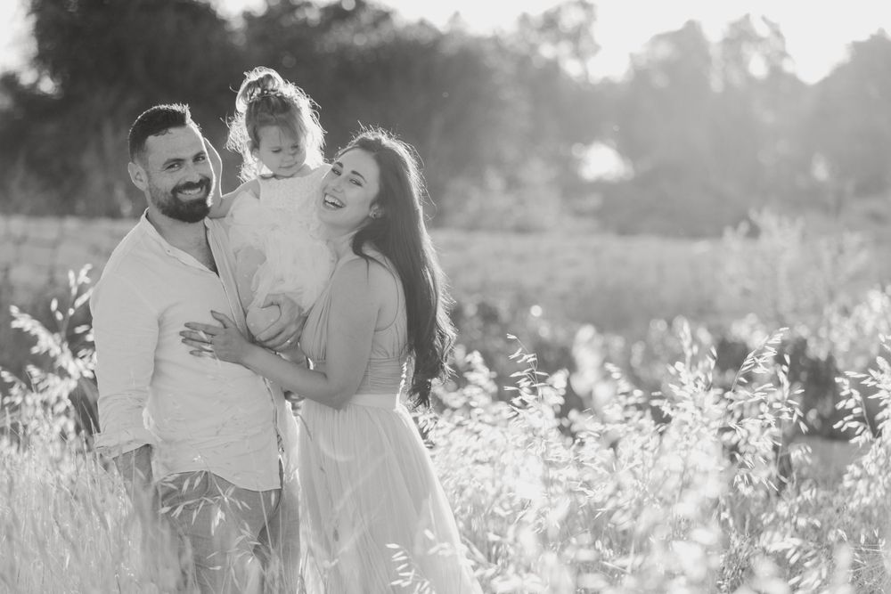 Couple embraces in a sunlit field of tall grass during golden hour.