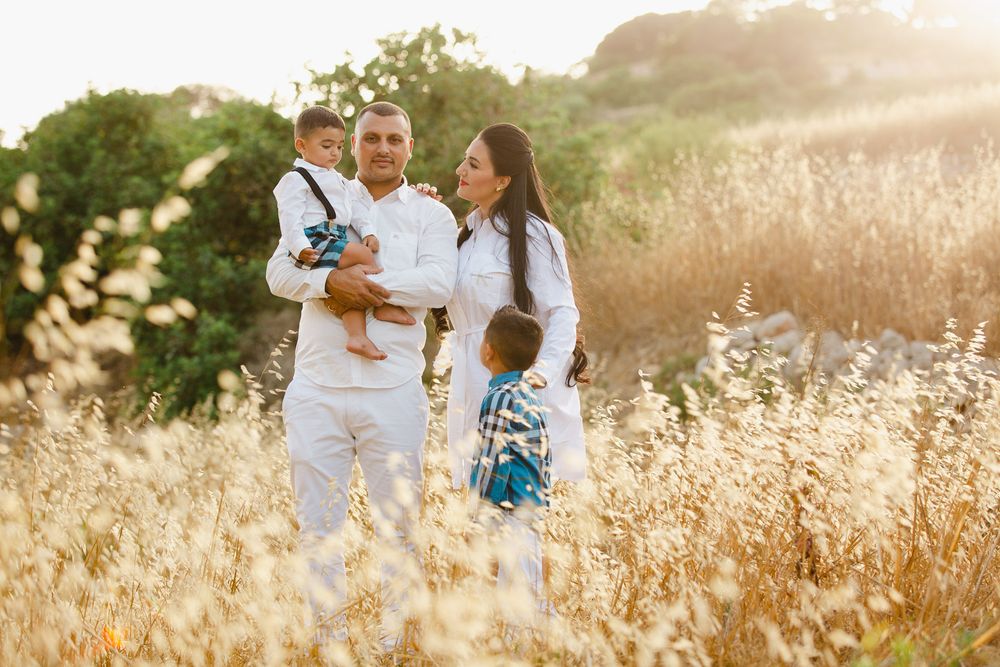 A couple and their child walk through a sunlit field of tall golden grass during a summer evening photo session.