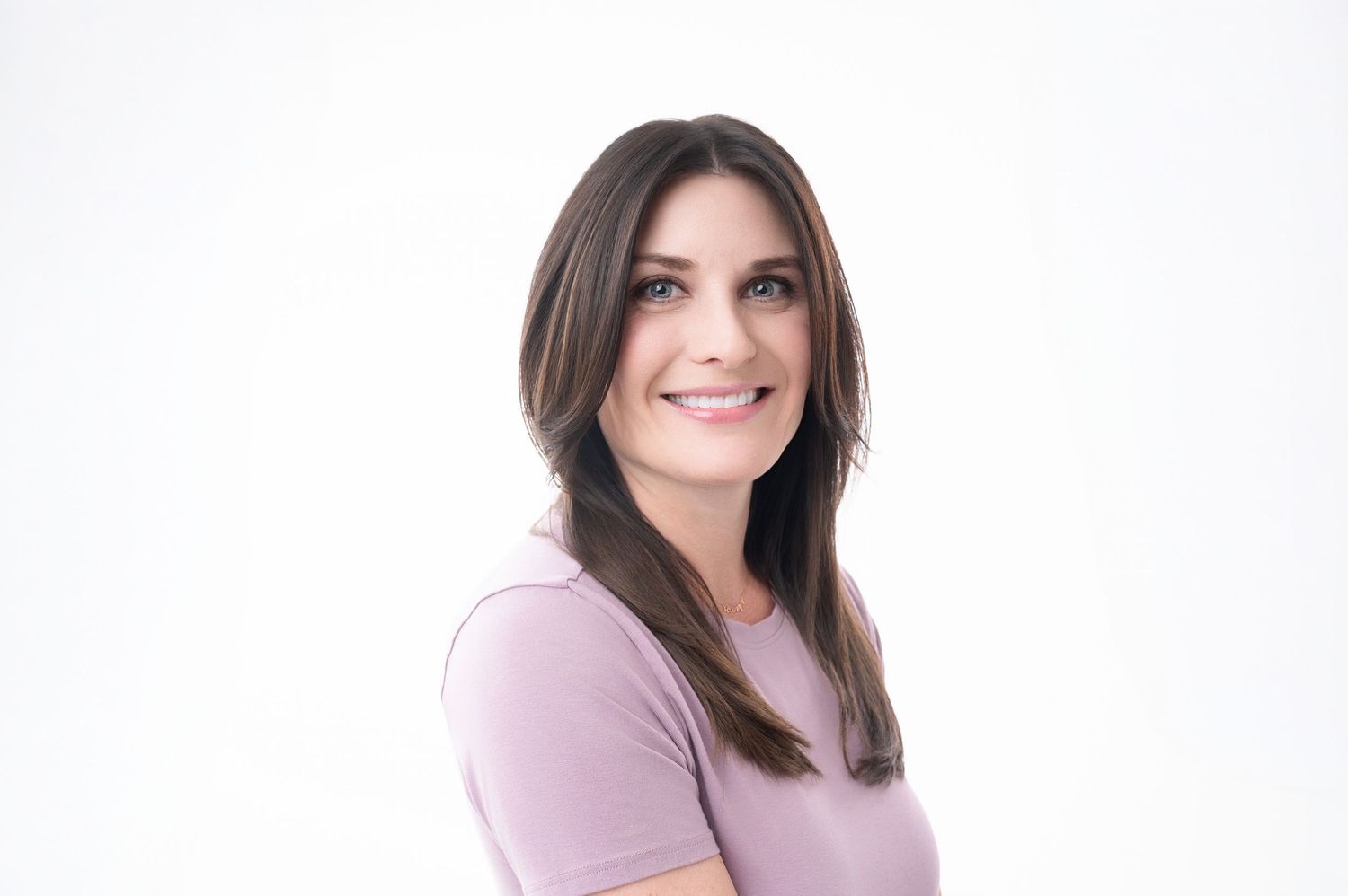 Professional headshot against white background of person in pink shirt smiling warmly.