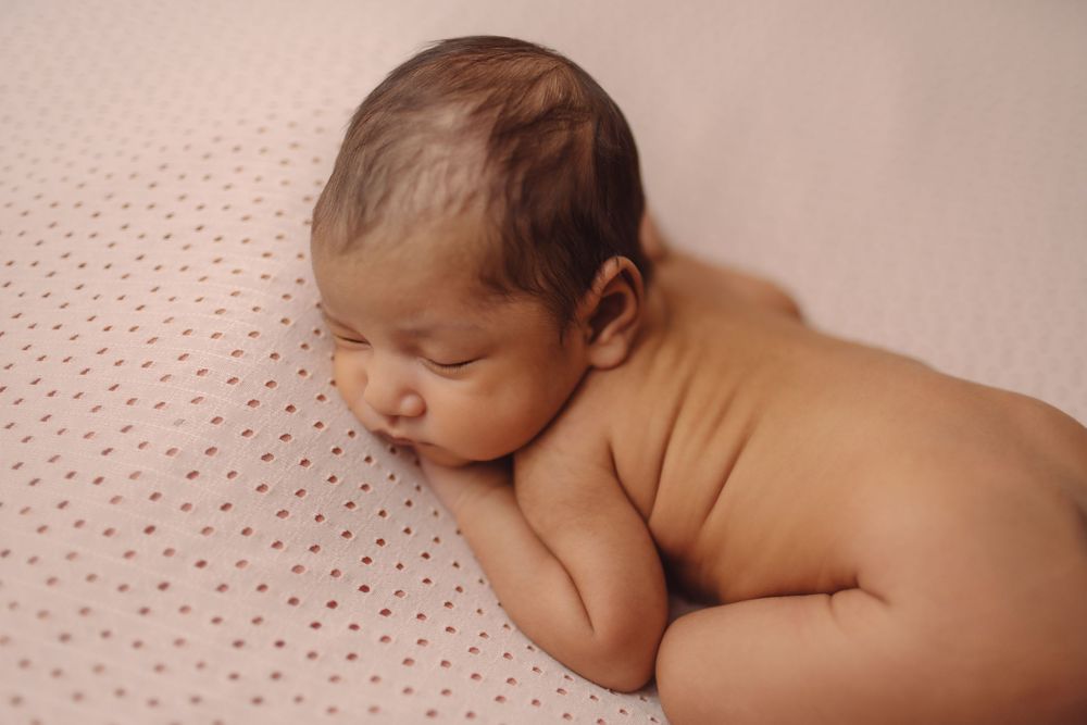 Peaceful newborn baby sleeping on a soft pink polka dot blanket in a curled position.