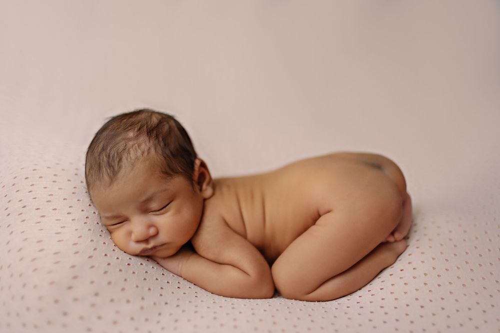 Peaceful newborn baby sleeping curled up on a soft pink blanket in a professional studio portrait.