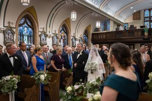 Bride walking down the aisle in a church wedding ceremony with guests standing in decorated pews.