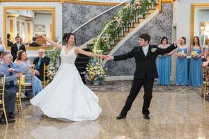 Bride and groom share first dance at elegant wedding reception with guests in blue attire seated nearby.