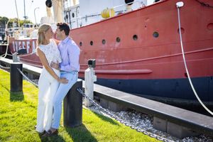 Couple kissing near a red boat docked at a marina on a sunny day.