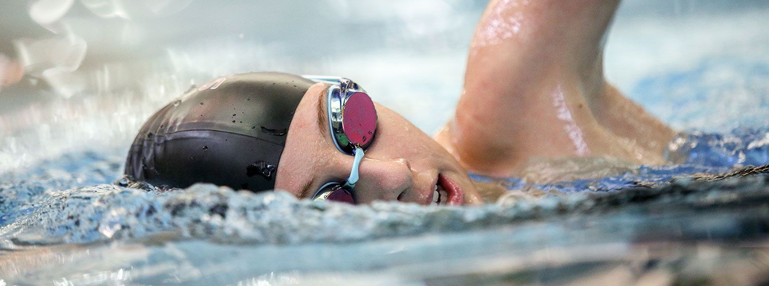 Close-up view of an NPA swimmer performing freestyle stroke in blue pool water wearing a swim cap and goggles.