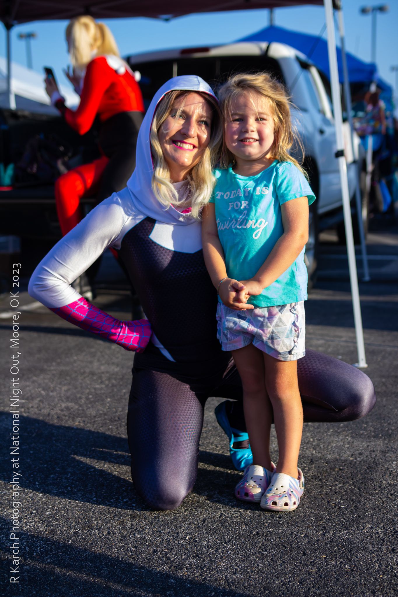 Costumed character in white and black outfit poses with young fan at outdoor event.