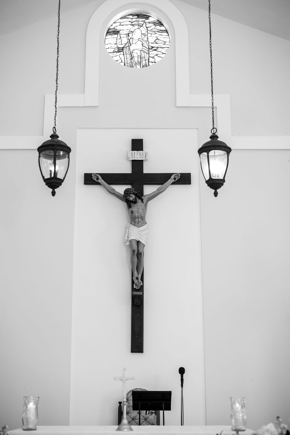 Black and white photo of a crucifix mounted on white wall with hanging lanterns.