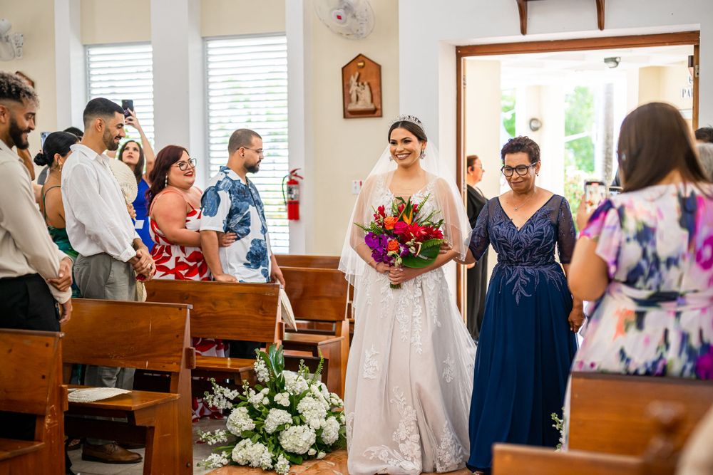 A wedding ceremony in a church with guests seated in wooden pews and white floral arrangements along the aisle.