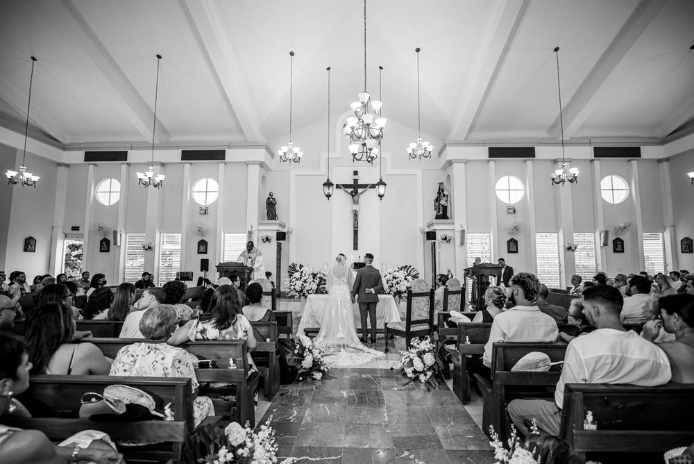 Black and white photo of a church wedding ceremony with guests seated in rows under pendant lighting.