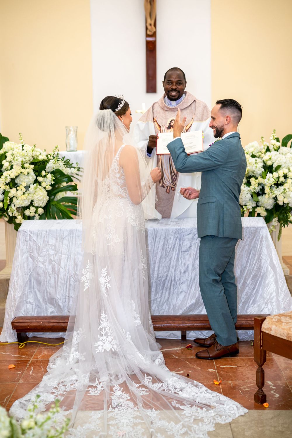 Traditional Catholic wedding ceremony with white floral arrangements and a long lace train.