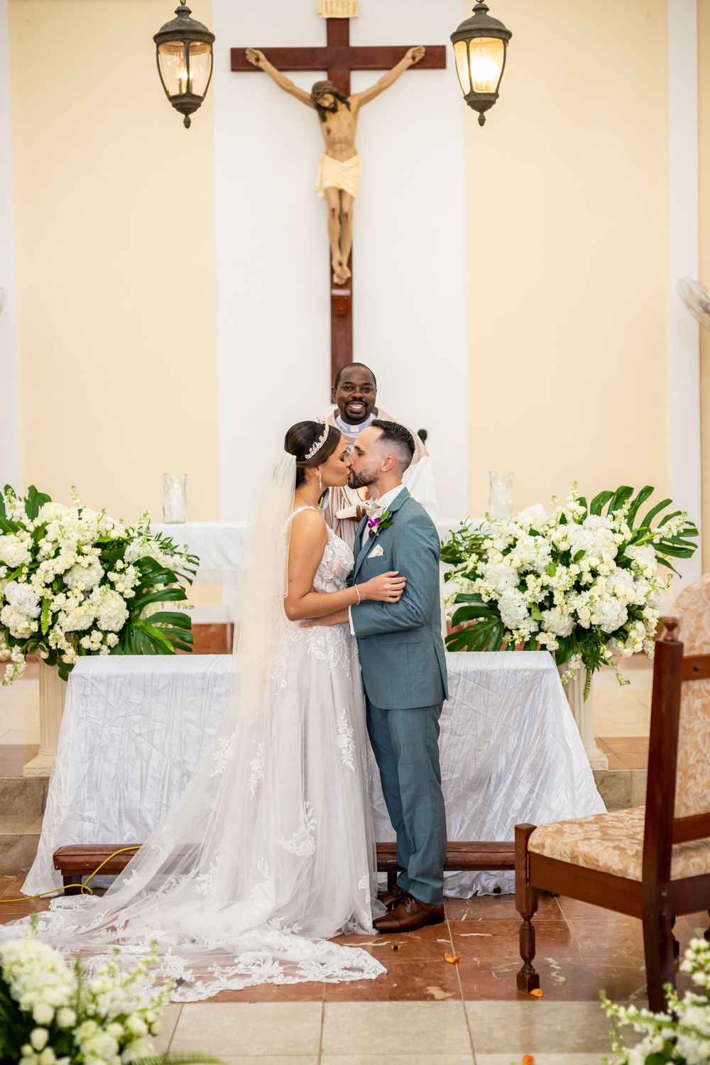 Wedding ceremony finale beneath a crucifix with ornate lanterns and white floral arrangements.