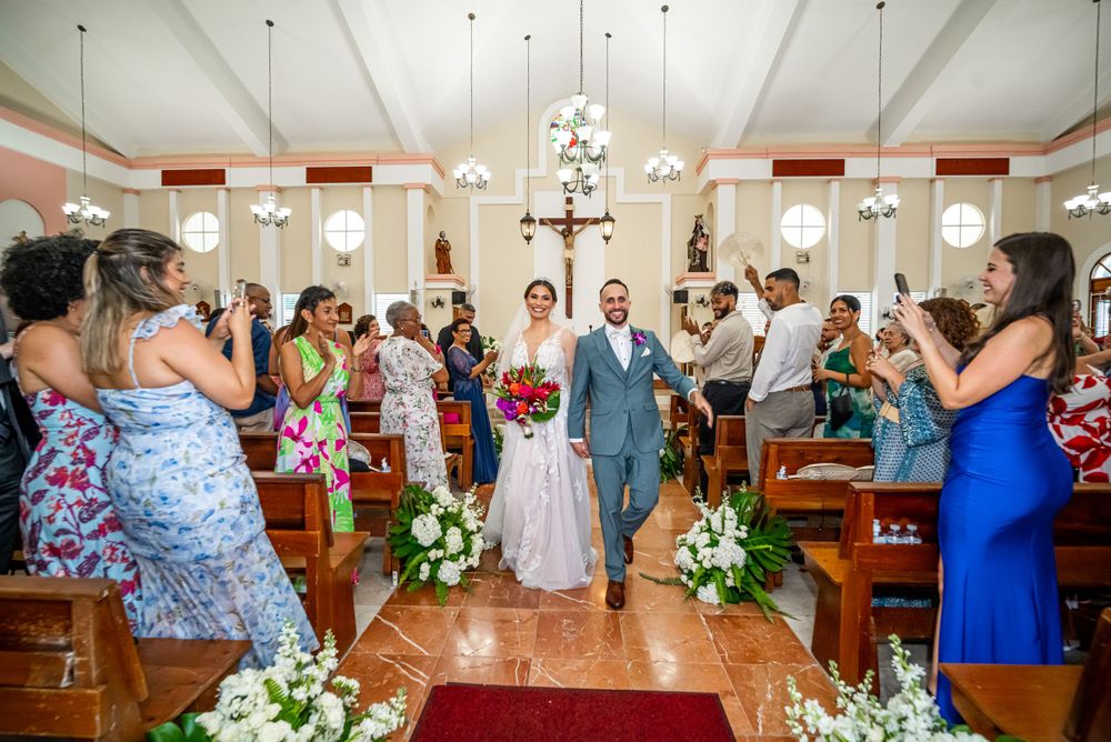 A couple walks down the church aisle after their wedding ceremony while guests take photos.