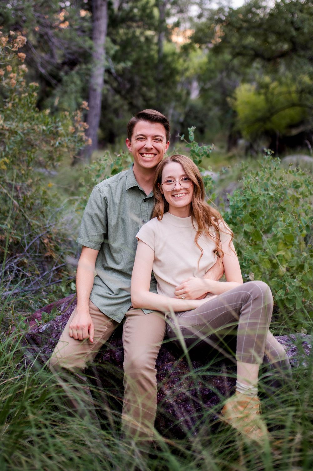 Happy young couple sitting together on rocks surrounded by lush green foliage outdoors.