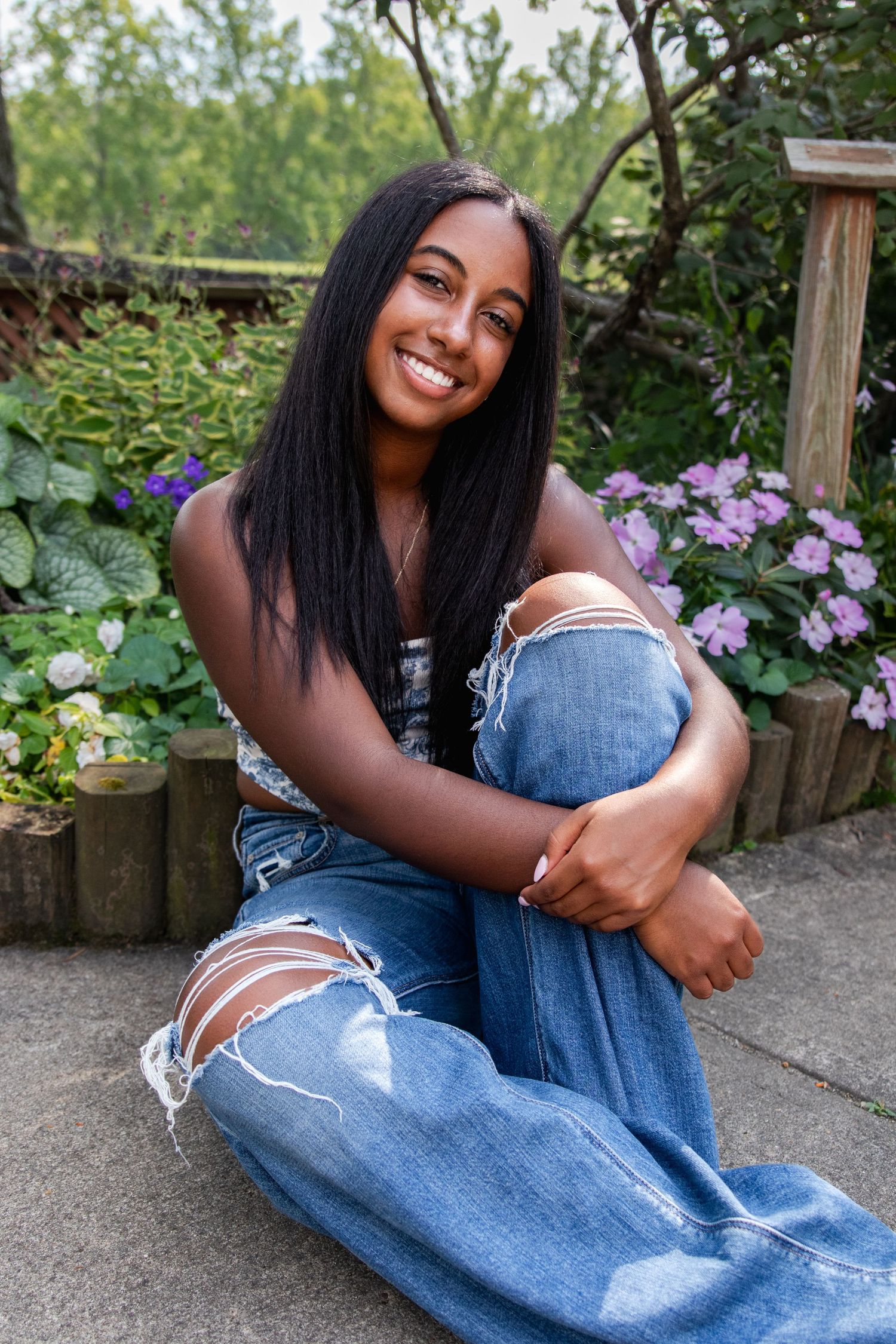 Candid garden senior photoshoot with purple flowers and wooden fence details.
